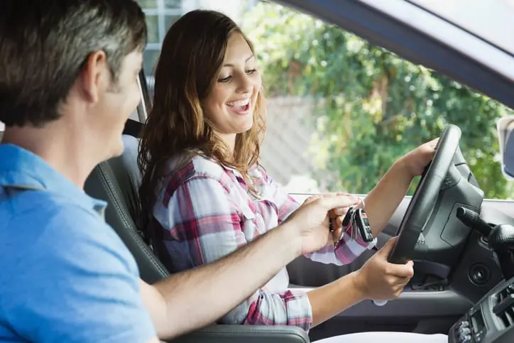 Carolina Collision and Frame Service | A father handing his smiling daughter keys to her first car as she sits behind the steering wheel